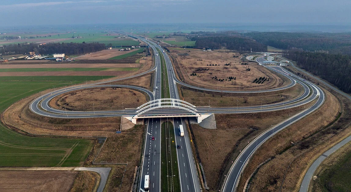 Widok z lotu ptaka na węzeł autostrady A2 Łyszkowice — dwa łukowate zjazdy łączące się w centralnym punkcie skrzyżowania, otoczone polami uprawnymi